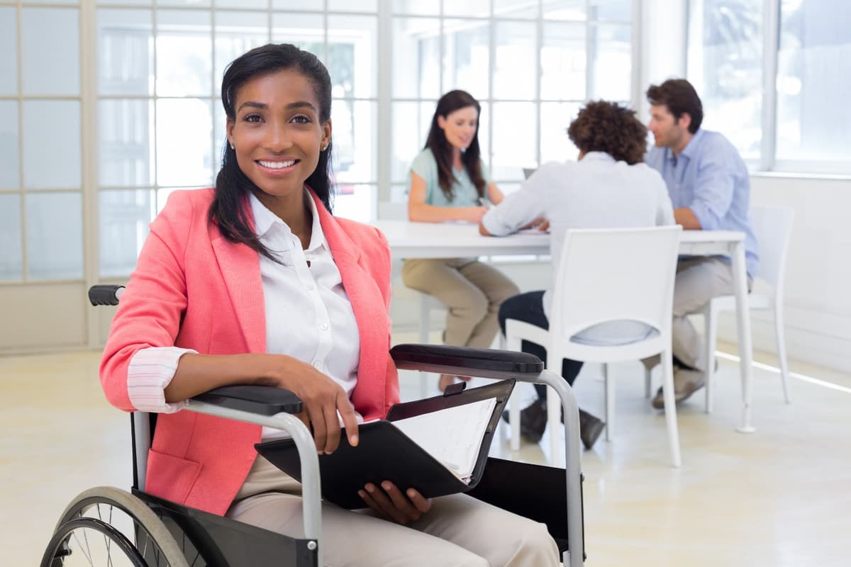 Profissional cadeirante sorrindo em ambiente corporativo com colegas ao fundo